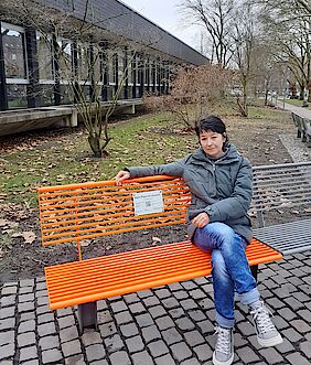 eine Mitarbeiterin der Frauen- & Mädchenberatungsstelle Schattenlicht sitz auf der orangen Bank vor dem Rathaus Wanne