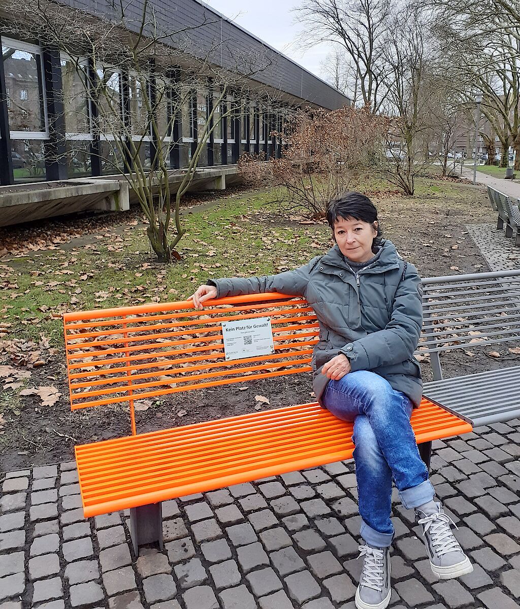 eine Mitarbeiterin der Frauen- & Mädchenberatungsstelle Schattenlicht sitz auf der orangen Bank vor dem Rathaus Wanne