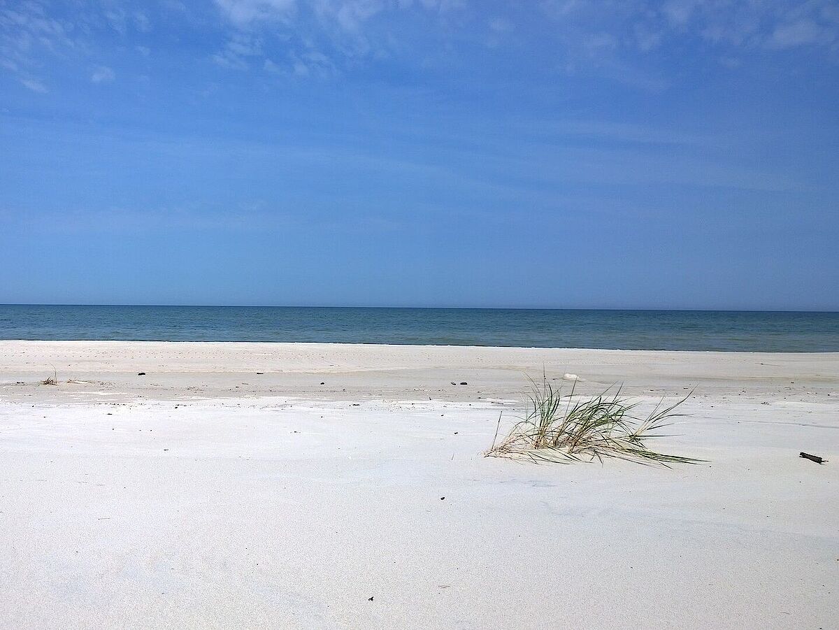 Foto eines weißen Strandes mit dunkelblauem Meer im Hintergrund